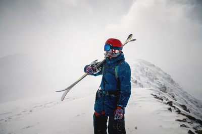 The skier holds a pair of skis and looks at the snow-capped mountains. a guy with skis on his