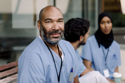 Portrait of confident male nurse sitting by colleagues outside hospital