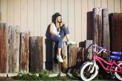 Trendy woman sitting on wooden posts at yard