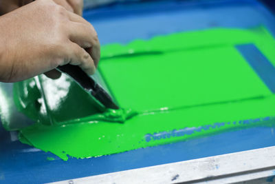 Cropped hands of person applying green ink on silk screen while working at workshop