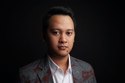 Portrait of young man standing against black background