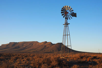 Windmill on land against clear blue sky