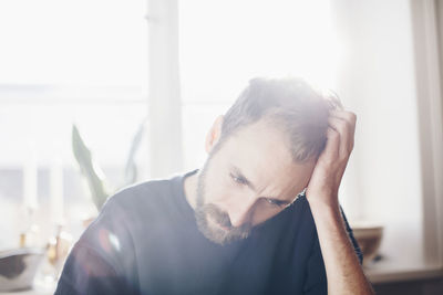 Worried man sitting with head in hands against window at home