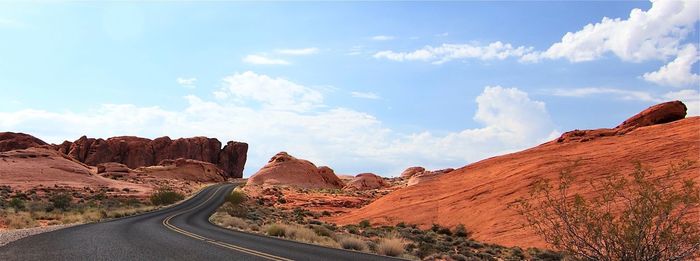 Empty road amidst rock formation against sky on sunny day