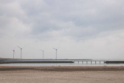 Wind turbines by sea against sky