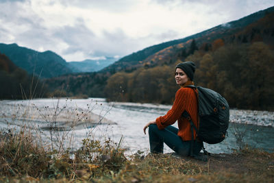 Woman sitting on mountain against sky