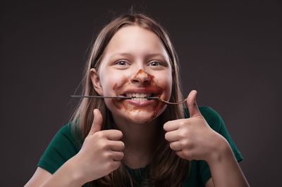 Portrait of young woman with sauce on face showing thumbs up sign against black background