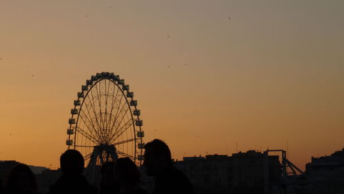 Silhouette people by ferris wheel against sky during sunset