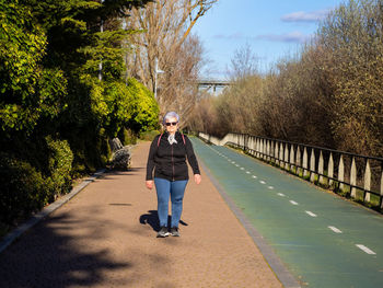 Full length portrait of senior woman walking on footpath amid trees