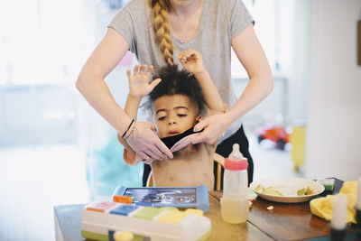 Midsection of mother dressing son at table