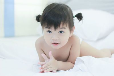 Portrait of cute baby girl sitting on bed