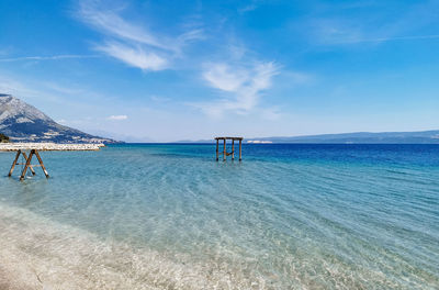 Beautiful blue sea with wooden swings in shallow water on beach.