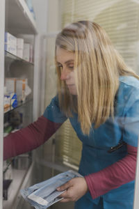 View through glass of young female doctor in uniform choosing instruments in medical case