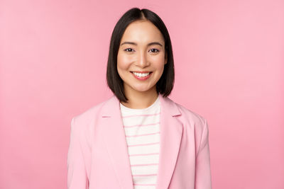 Portrait of young woman standing against pink background