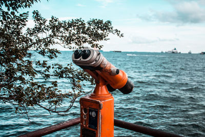 Close-up of coin-operated binoculars by sea against sky