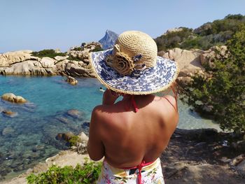 Rear view of shirtless man standing on rock by sea