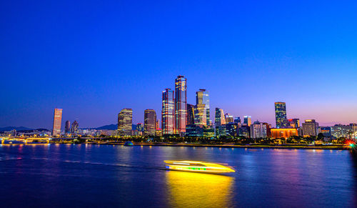 Illuminated city buildings against clear blue sky