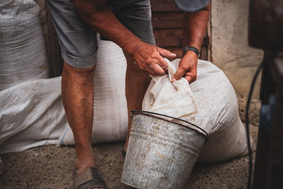 An elderly man pours wheat from a bag into a bucket.
