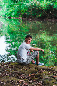 Portrait of man sitting by lake in forest