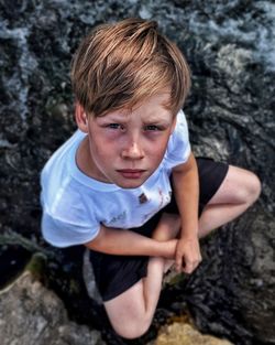 High angle portrait of boy sitting on fallen tree