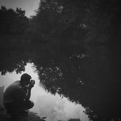 Rear view of people photographing lake against trees