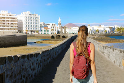 Rear view of woman with backpack walking in city against sky