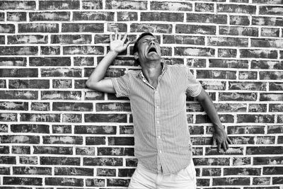 Man making face while standing against brick wall