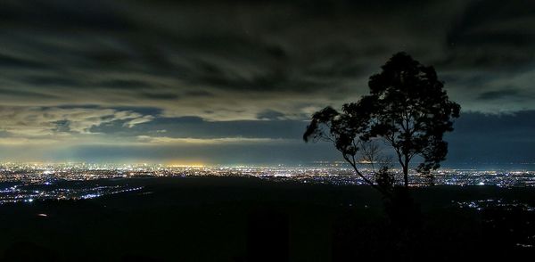 Illuminated cityscape against cloudy sky at night