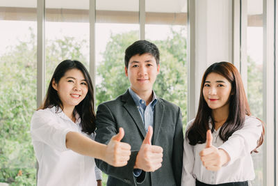 Portrait of business colleagues showing thumbs up against window in office