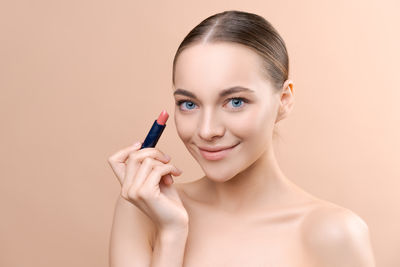 Close-up of young woman applying make-up against pink background