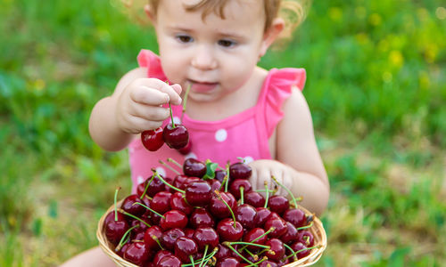 Cute baby girl with berries sitting on grass