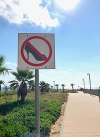 Road sign on footpath against sky