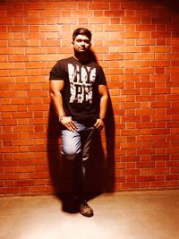 Portrait of young man standing against brick wall