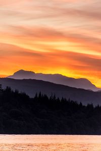 Scenic view of mountains by lake against cloudy sky during sunset