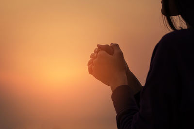 Midsection of woman with hands clasped
 against sky during sunset