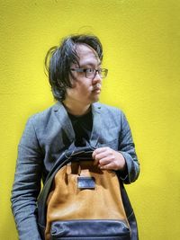 Portrait of young asian man standing against yellow background.