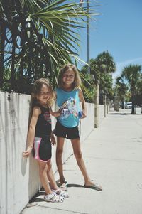 Full length portrait of siblings standing by wall on street during sunny day