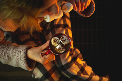 Directly above shot of woman eating marshmallows while holding coffee cup