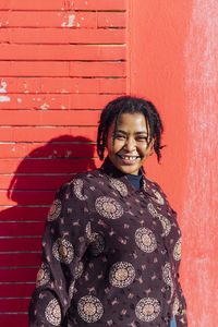 Portrait of smiling woman standing against red wall