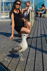 Woman wearing sunglasses crouching by bird on pier