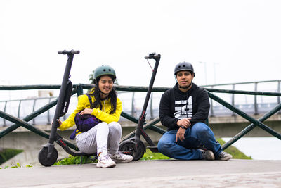 Portrait of smiling coupe sitting on push scooter against clear sky