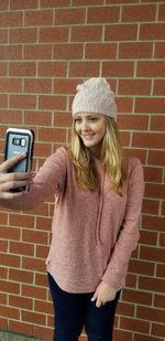 Portrait of young woman wearing hat standing against brick wall