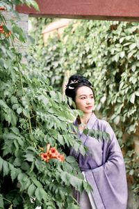 Portrait of young woman standing by plants