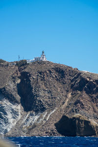 Lighthouse on rock by sea against clear blue sky