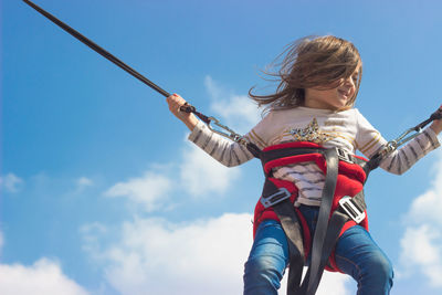 Low angle portrait of girl enjoying bungee jumping against sky