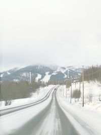 Snow covered road by trees against sky