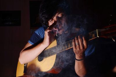 Man smoking cigarette while playing guitar in darkroom