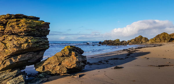 Panoramic view of rocks on beach against blue sky