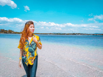 Portrait of smiling young woman standing on beach against sky