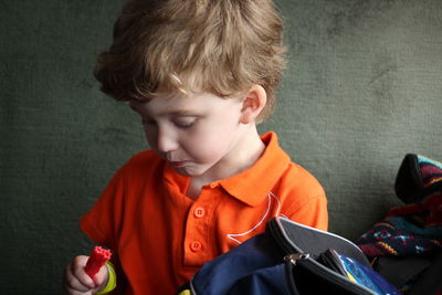 Close-up of boy holding felt tip pen while sitting against wall